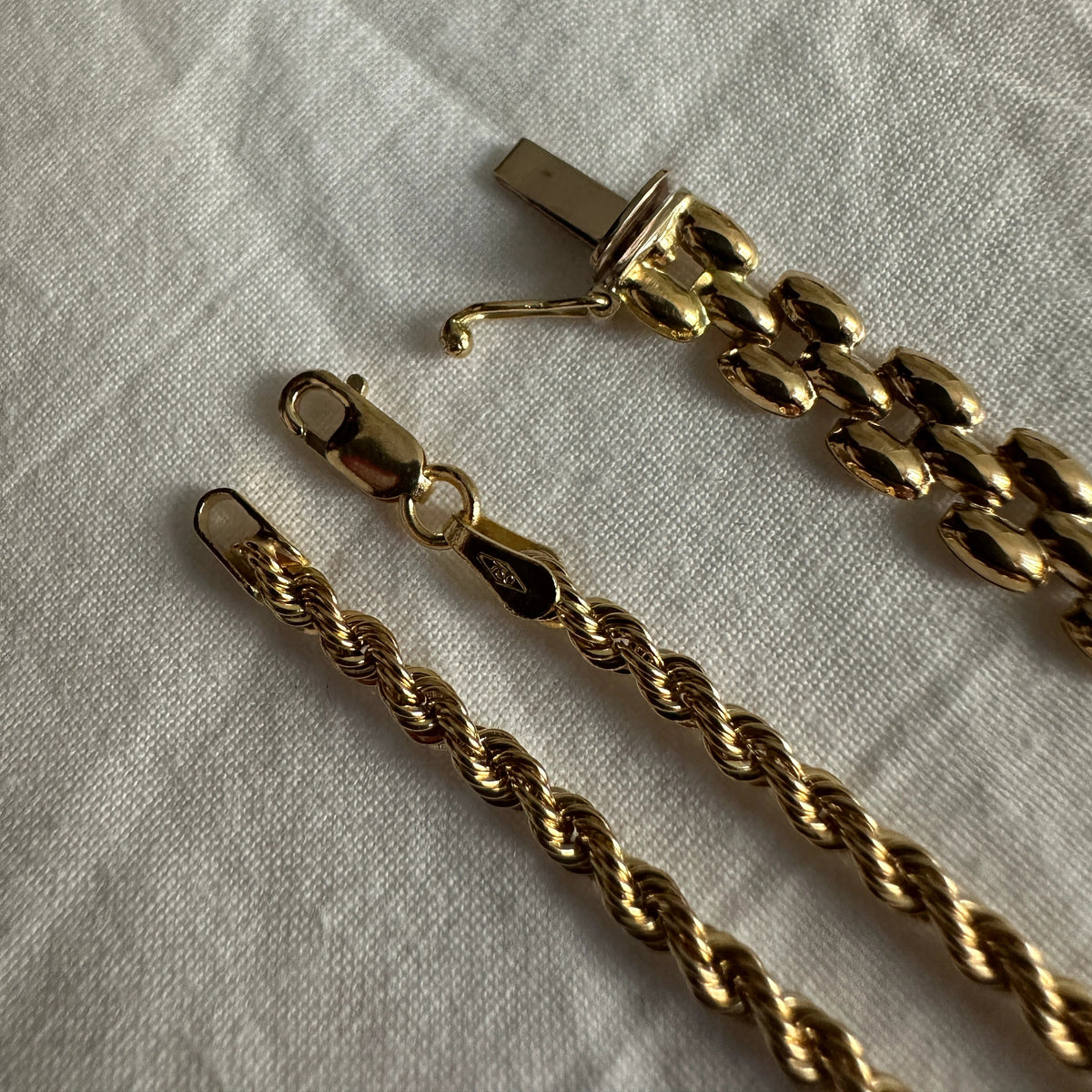 Two 18k gold pieces laid on a light gray fabric background: a twisted rope chain and a panther link with a lobster clasp.