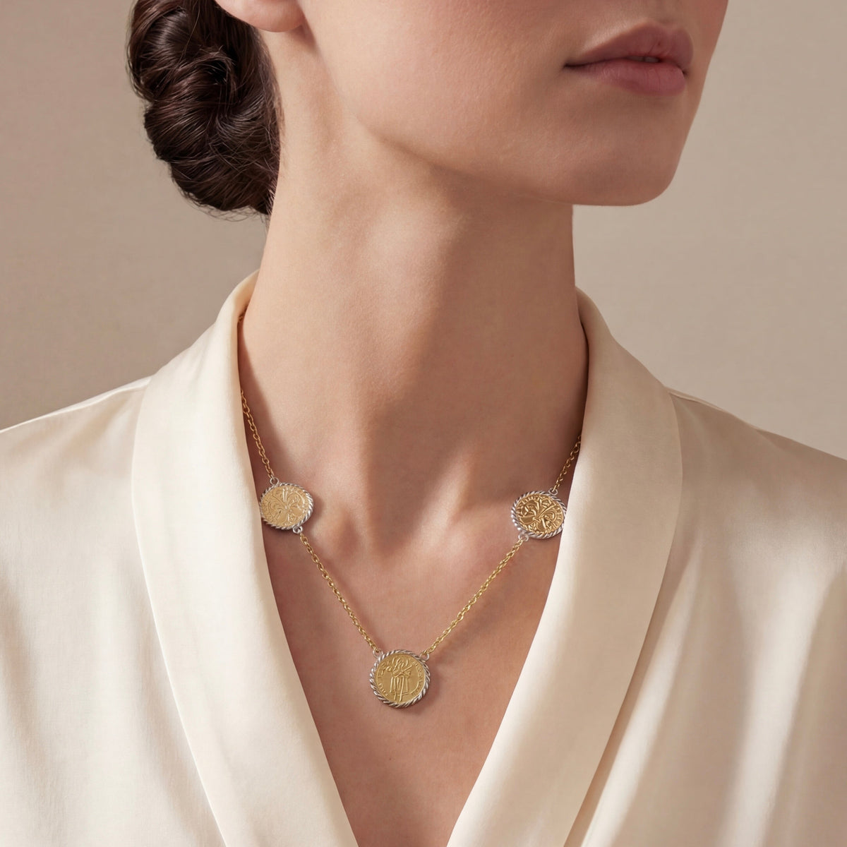 A close-up of a model wearing a delicate 18k Italian gold necklace with three florin coin, styled with a cream satin shirt against a neutral beige background.
