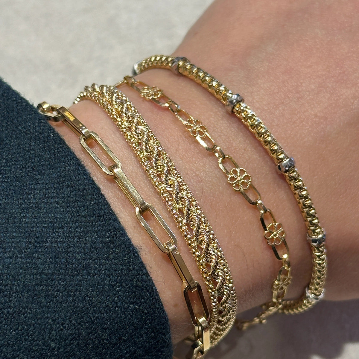 A close-up of a person's wrist wearing five stacked gold bracelets, including the Elastic bracelet.
