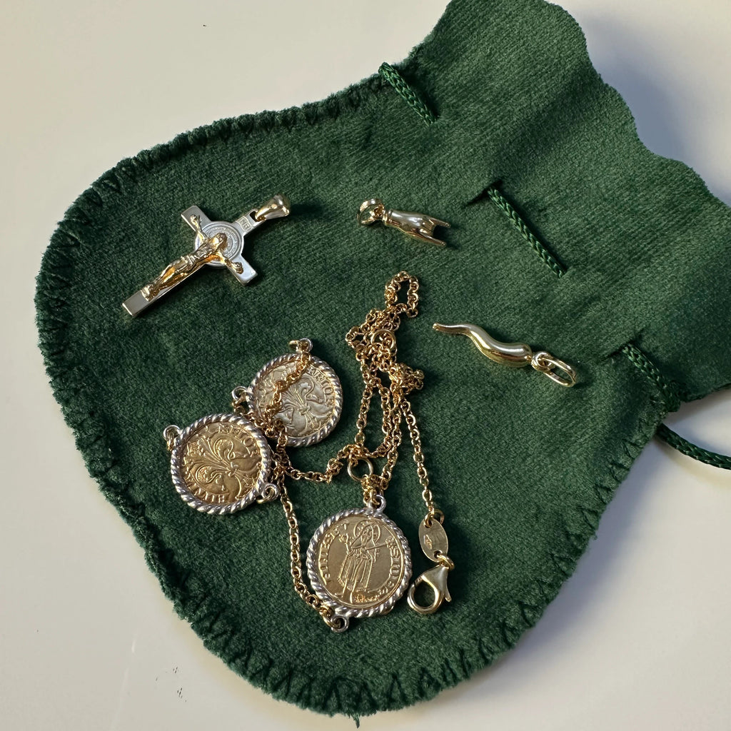 A collection of gold religious and lucky jewelry, including a crucifix and horns, as well as the 3-coin necklace, arranged on a dark green velvet drawstring pouch.