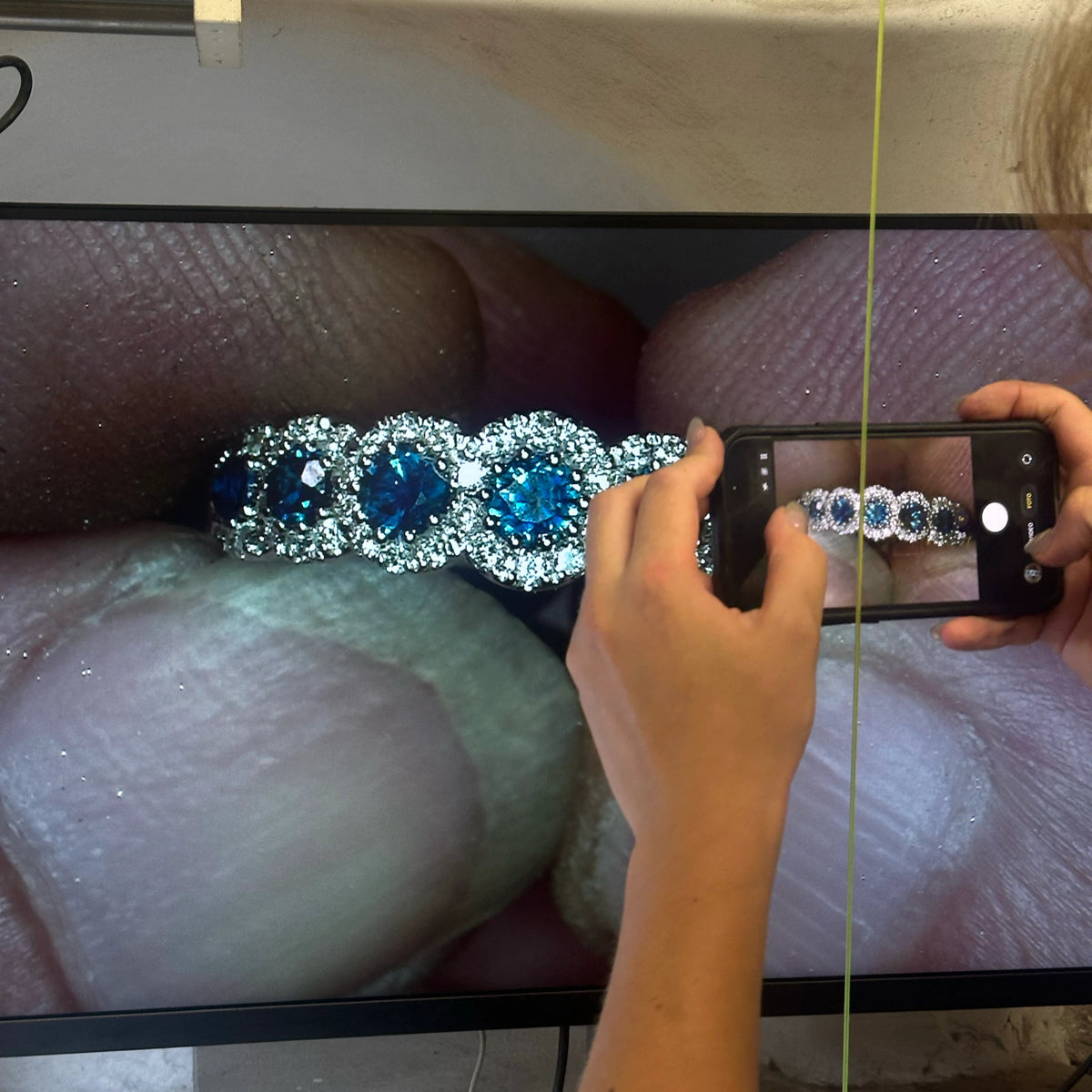 A close-up of the process of setting the precious stones in a delicate 18k gold ring, shown in a gem-setter's magnifying zoomed screen.