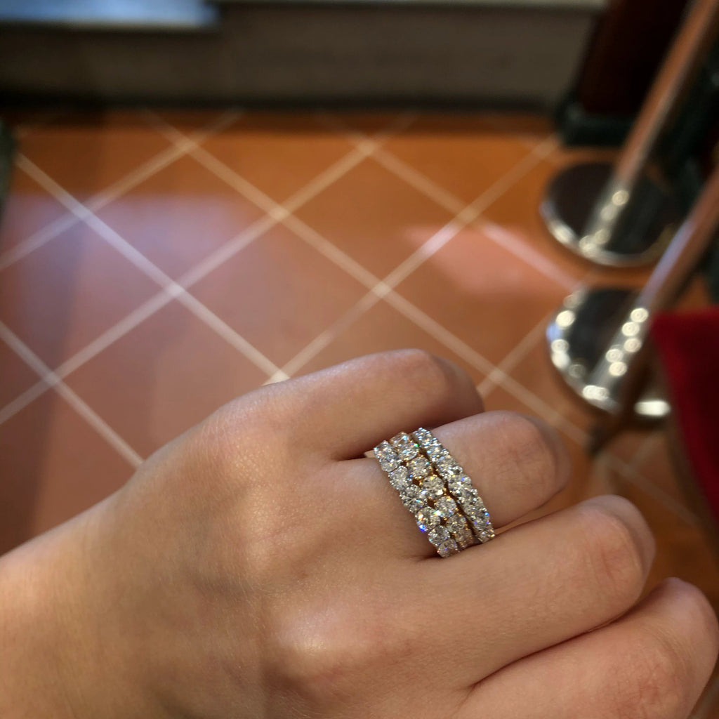 A close-up of a hand wearing a three-band diamond ring set in 18k white and yellow gold.