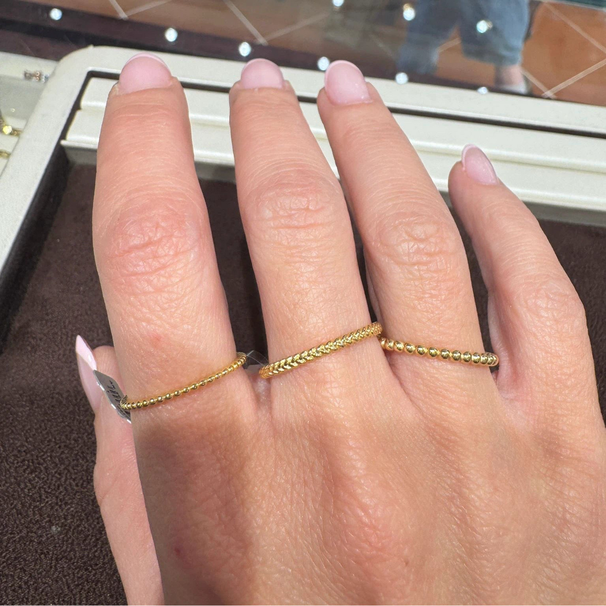 A close-up of a hand wearing three delicate gold rings. A twsited rope and beaded rings.