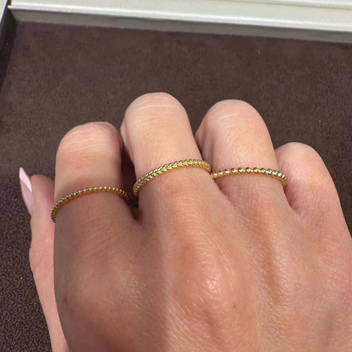 Three delicate gold rings worn on a person's fingers, shown in a close-up shot