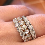 A close-up of three gold diamond ring worn on a finger. The ring features three parallel rows of round-cut diamonds set in yellow gold or white gold.